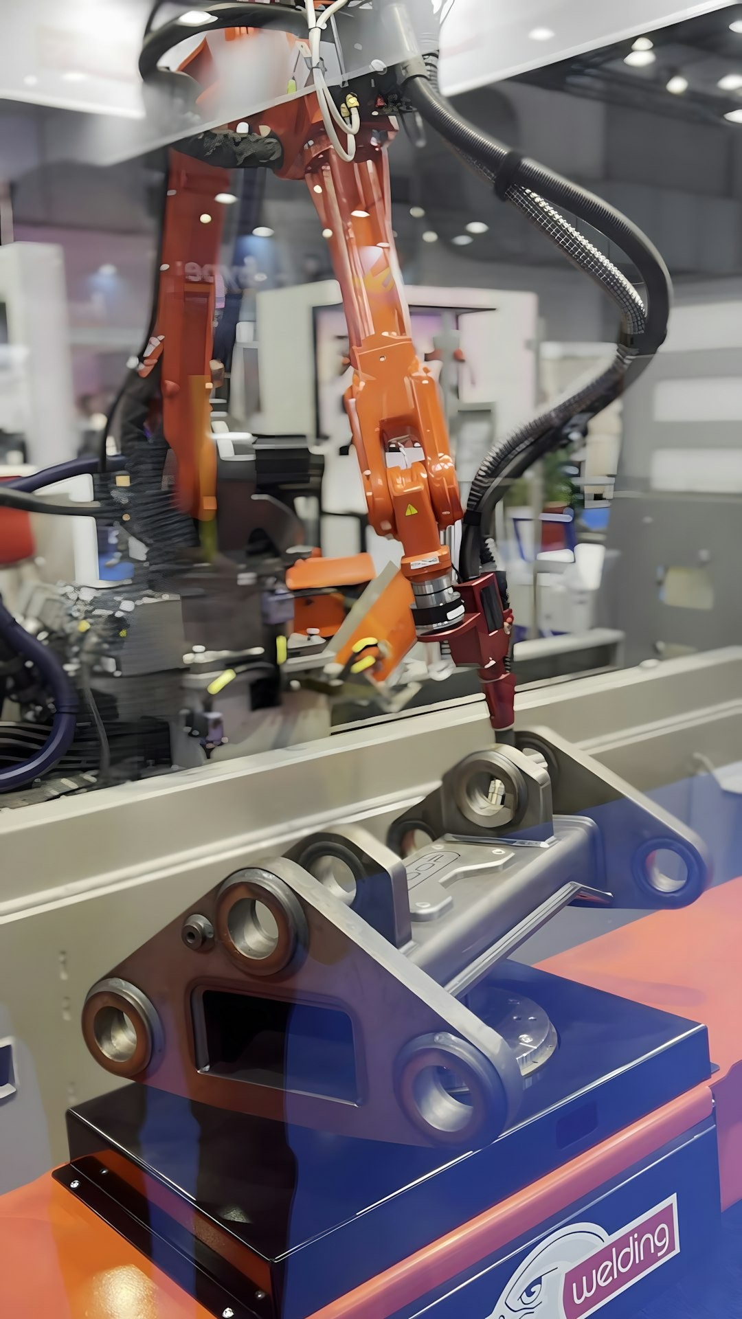 Orange robotic arm lowers to grasp metal machine part.